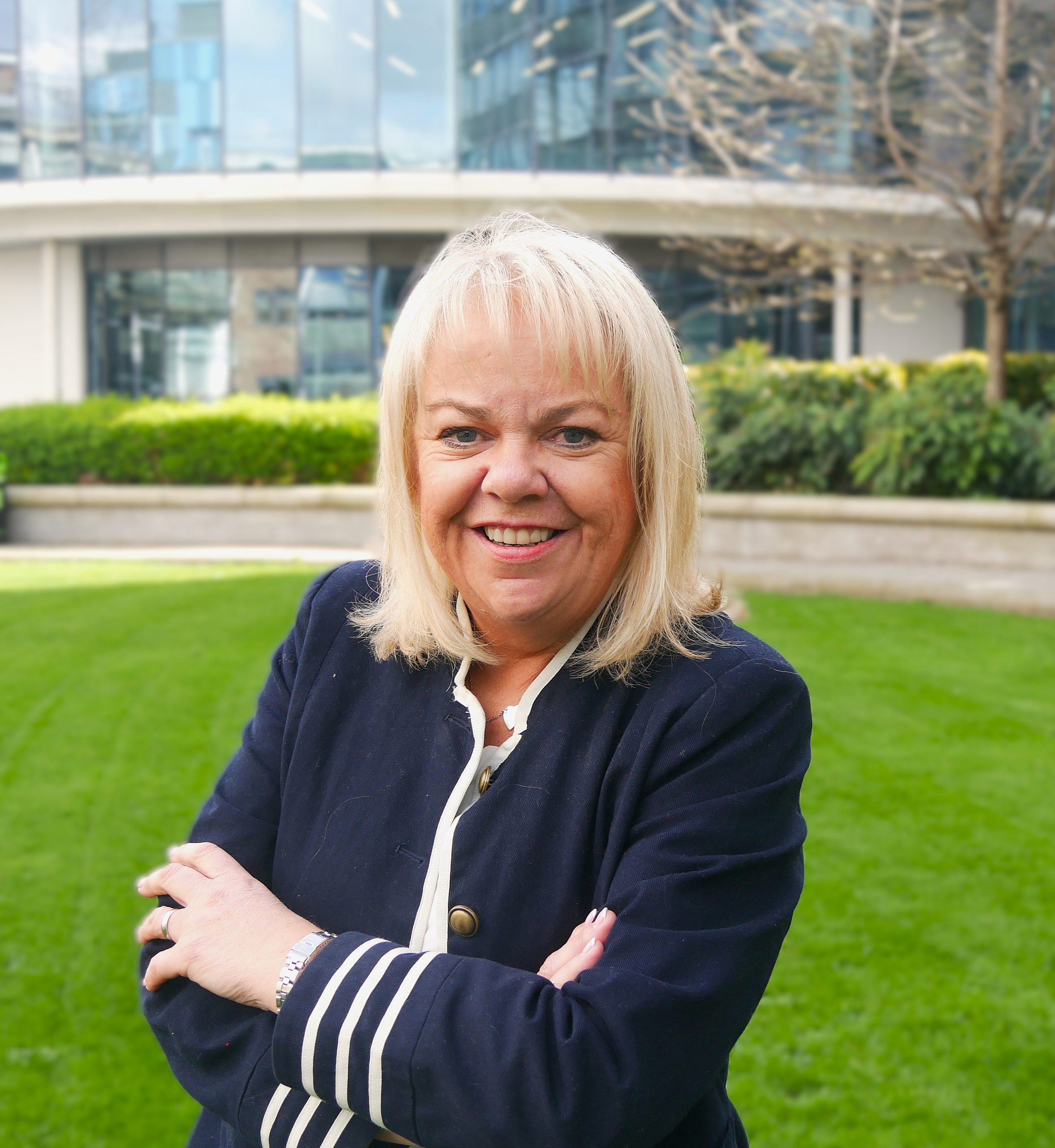 woman with light blond hair wearing navy jacket and a white shirt with her arms folded