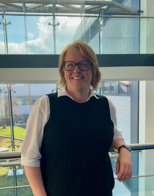 a medium shot of a white woman with short blond hair and glasses